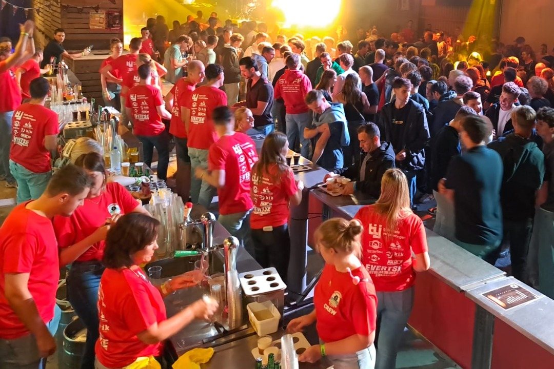 Vrijwilligers in rode shirts achter de tap